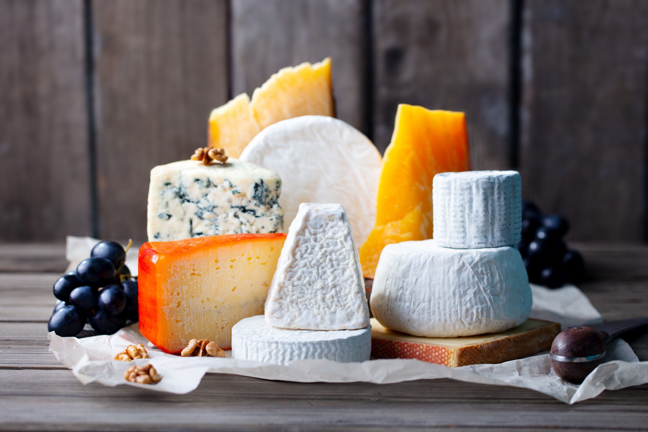 Cheese assortment: blue cheese, hard cheese, soft cheese on a parchment paper. Wooden backgroun
